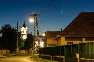 comet NEOWISE from a lit town in blue hour Hungary